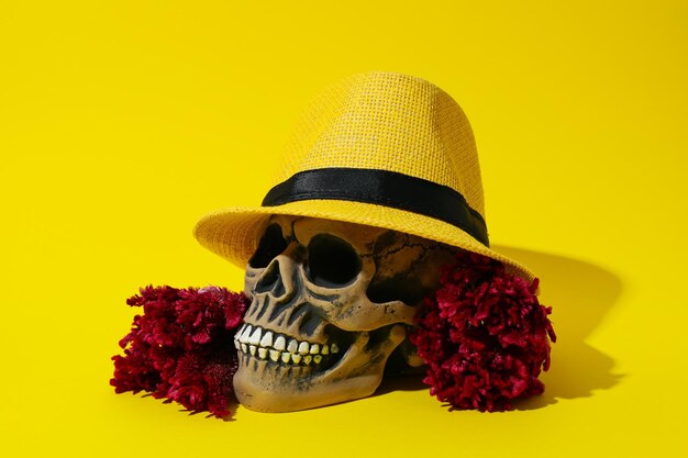 Calavera con sombrero y flores sobre fondo amarillo