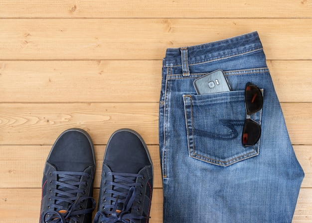 Foto calça jeans e acessórios masculinos no chão de madeira.