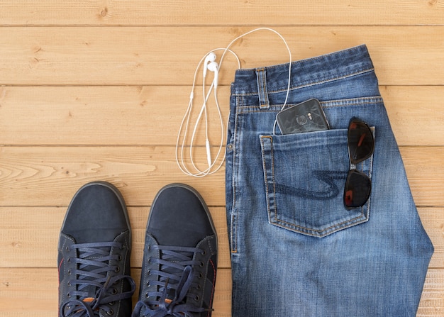 Calça jeans e acessórios masculinos no chão de madeira.