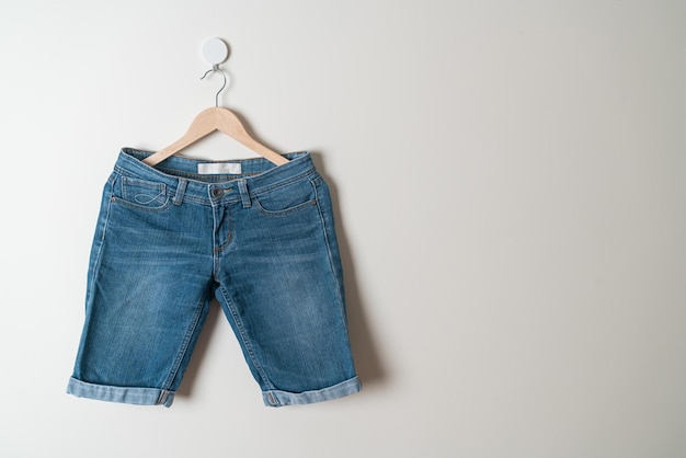 calça jeans pendurada com cabide de madeira na parede