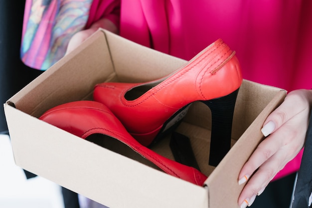 Foto calçado elegante e moderno. conceito de compras e estilo de vida. mulher com as mãos segurando elegantes sapatos de salto alto de couro vermelho em uma caixa.