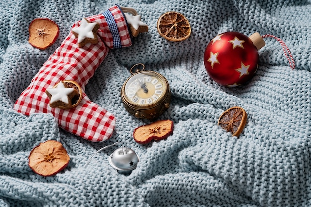 Calcetín navideño relleno de galletitas estrella y decorado con naranjas secas, reloj y juguete navideño sobre un plaid azul. Concepto de Navidad acogedor