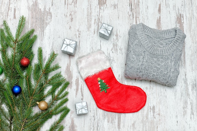 Calcetín rojo de Navidad y un suéter gris Rama de abeto decorada Fondo de madera Concepto de moda