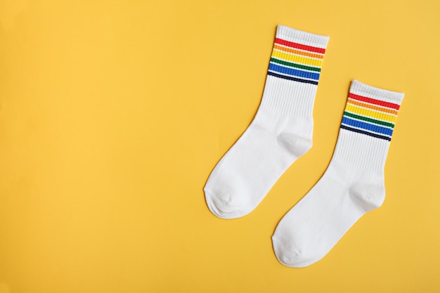 Calcetines de algodón blanco de vista superior con colores del arco iris sobre fondo amarillo Idea de regalo de símbolo LGBTQ