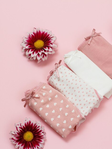 Calcinha de algodão dobrada de cor diferente com botões de flores de áster em fundo rosa. Conjunto de roupa interior de mulher. Vista do topo.