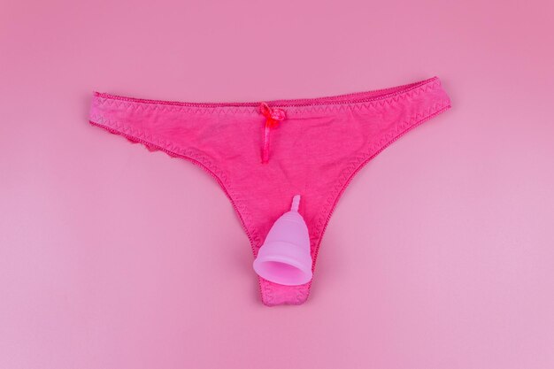 Calcinha feminina com copo menstrual em fundo rosa pastel Vista superior Conceito de higiene feminina de menstruação em dias críticos