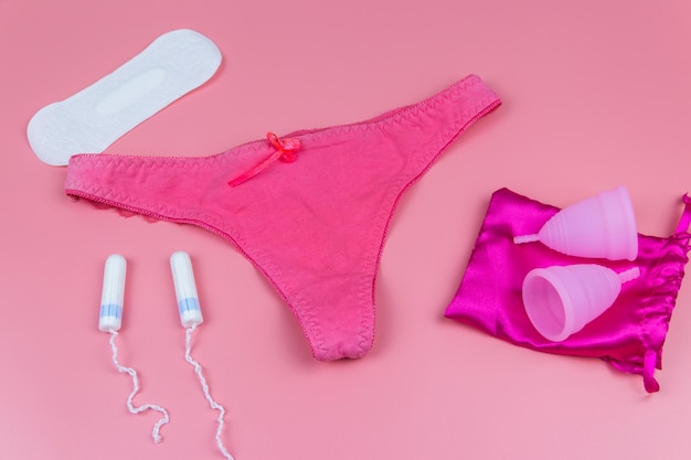 Calcinhas femininas com absorventes higiênicos e absorventes menstruais em fundo rosa pastel Conceito de dias críticos menstruação higiene feminina