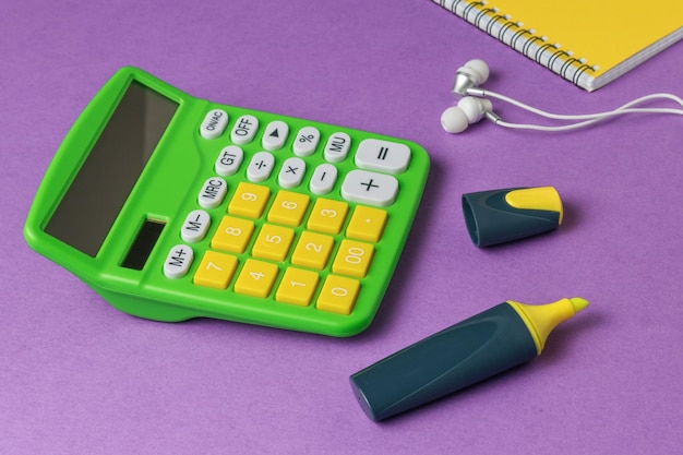 Calculadora de auriculares con marcador amarillo y un cuaderno sobre un fondo morado