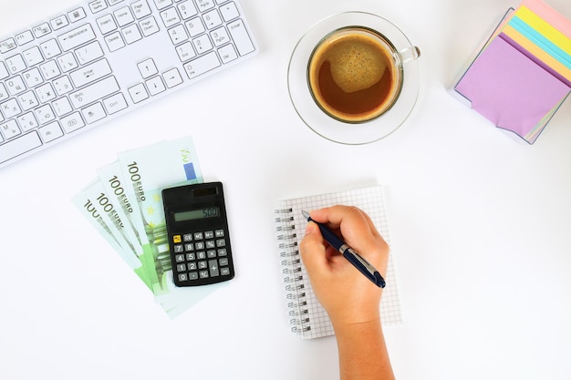 Calculadora, billetes de banco del euro, cuaderno en una mesa a una taza de café y un teclado.