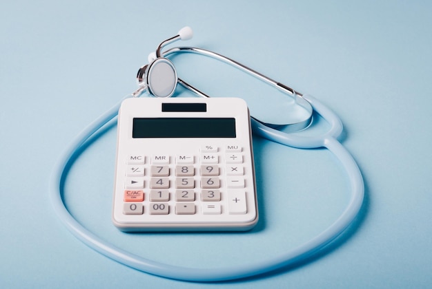 Calculadora blanca y estetoscopio azul sobre un fondo azul como símbolo de la medicina pagada (cara)