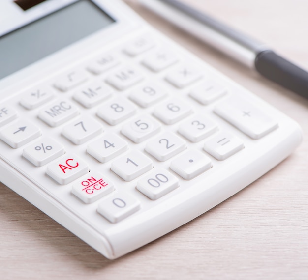 Calculadora branca e caneta na análise de mesa de madeira brilhante e estatísticas do conceito de risco de investimento de lucro financeiro cópia espaço macro close-up