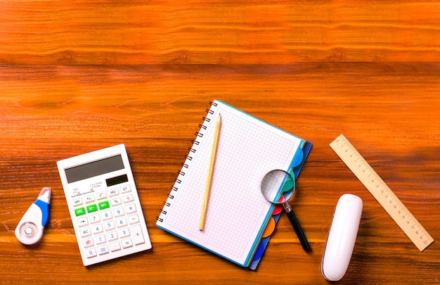 Foto calculadora, caderno com uma mola, régua, lupa, lápis, grampeador em uma mesa de madeira