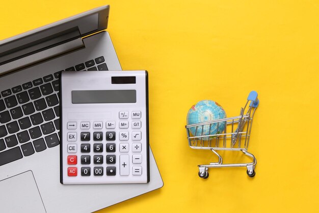 Calculadora y carrito de compras con globo portátil sobre fondo amarillo Vista superior