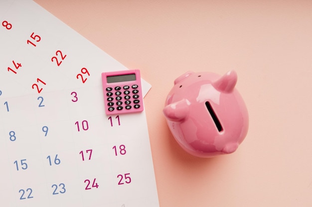 Calculadora com calendário e cofrinho no conceito de economia de dinheiro de objetivo financeiro de imposto de fundo rosa