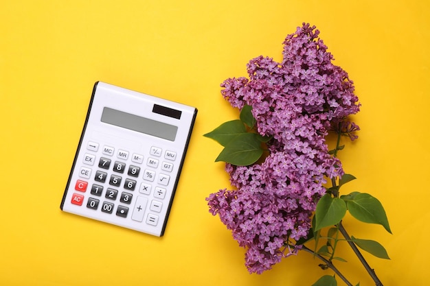 Calculadora com ramo de lilás florescendo em fundo amarelo Vista superior Flat lay