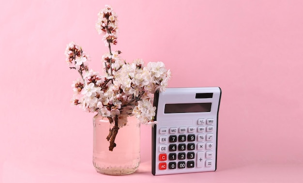 Calculadora e belos ramos floridos em frasco de vidro em fundo rosa