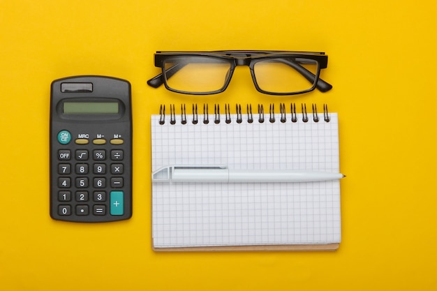 Calculadora e óculos clássicos, caderno em um amarelo.