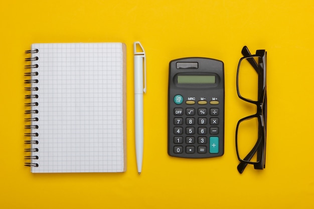 Calculadora e óculos clássicos, caderno em um amarelo.