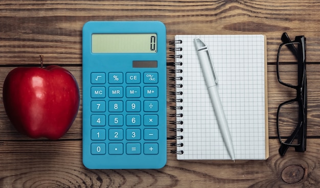 Calculadora con manzana roja, cuaderno, vasos de madera