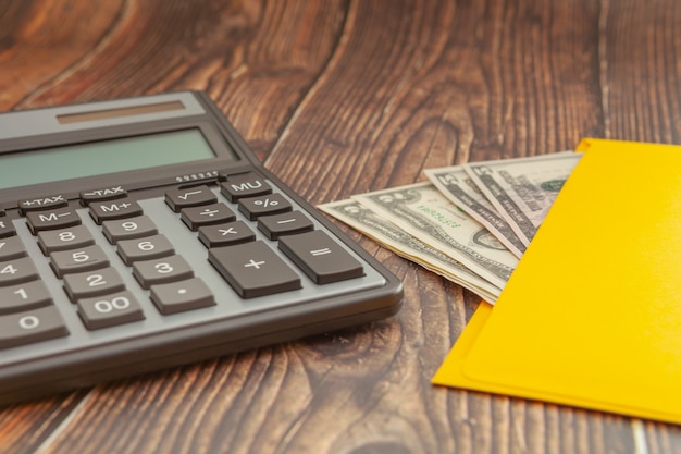 Foto calculadora moderna em uma mesa de madeira com um envelope amarelo e dinheiro