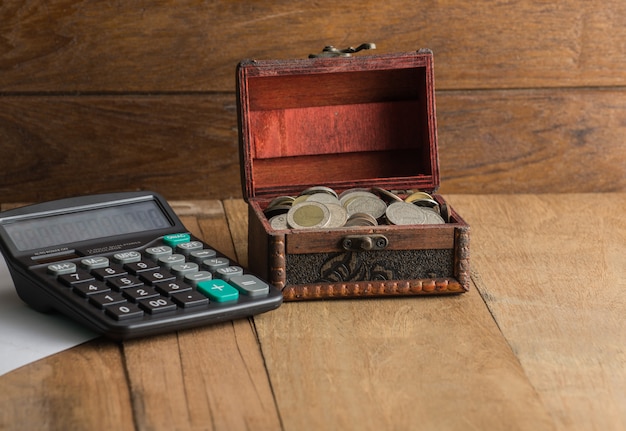 Calculadora con moneda en un cofre sobre fondo de madera