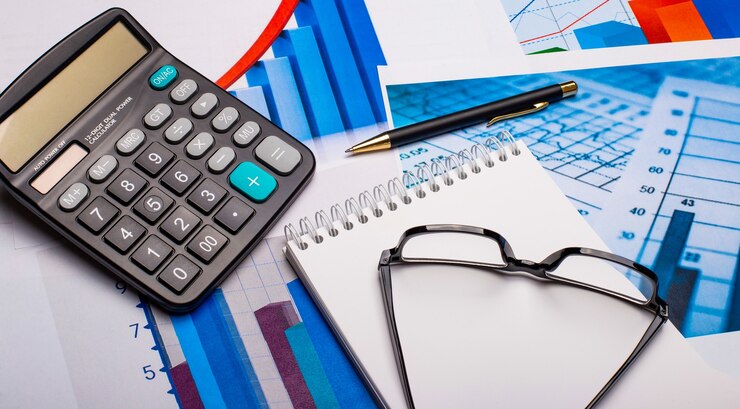 Foto calculadora, óculos, bloco de notas branco e caneta em diagramas brilhantes. local de trabalho de perto