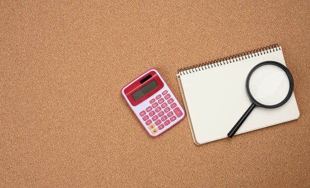 Calculadora rosa, cuaderno con hojas blancas en blanco y lupa negra sobre un fondo marrón. Banner para negocios, vista superior