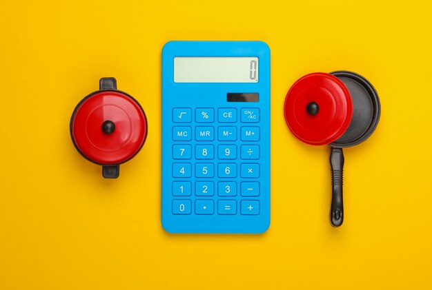 Cálculo del costo de cocinar. Sartenes calculadora y juguete sobre un fondo amarillo. Vista superior. Minimalismo