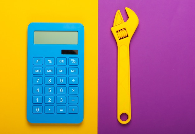 Cálculo do custo da obra de reparo. Calculadora e chave inglesa de brinquedo em fundo amarelo roxo. Vista do topo