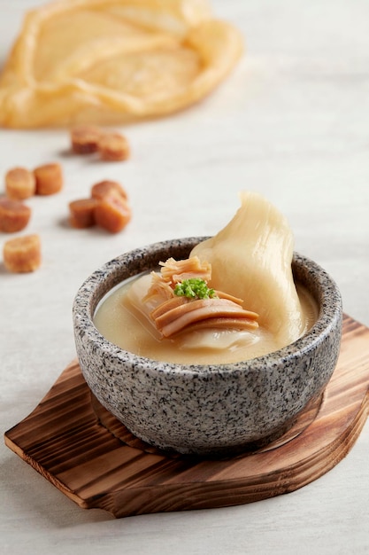 Caldo de galinha tradicional com peixe maw servido em pote de pedra japonês servido em um prato isolado em fundo cinza