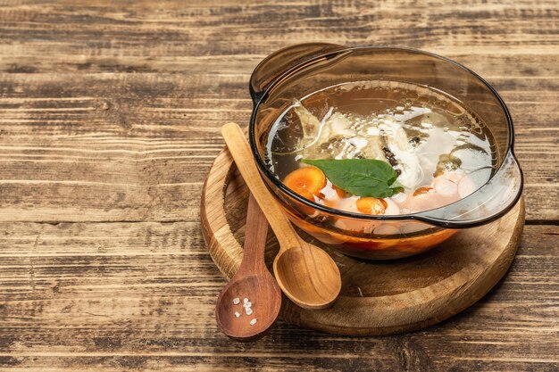 Caldo de galinha transparente. Sopa clara com baixo teor de gordura com cenoura, verduras e especiarias. Prato quente, talheres, fundo de madeira velho, espaço de cópia