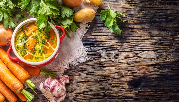 Caldo de sopa de galinha em uma tigela vintage com macarrão caseiro cenoura cebola aipo ervas alho e legumes frescos - topo da vista.