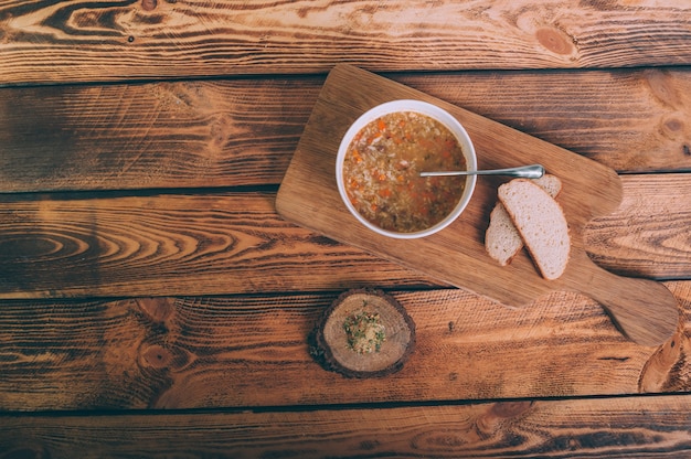 Caldo de sopa em uma tigela com pão sobre uma mesa de madeira.