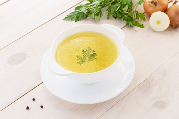 Caldo de huesos de pollo con perejil en un recipiente blanco sobre una mesa de madera