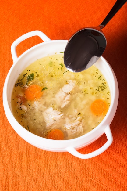 Un caldo de pollo en loza blanca sobre el mantel naranja