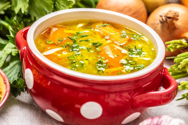 Caldo de sopa de pollo o verduras en un tazón vintage con fideos caseros, zanahoria, cebolla, apio, hierbas, ajo y verduras frescas.