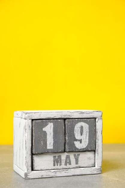 Foto calendario del 19 de mayo hecho con cubos de madera y fondo amarillo con un espacio vacío para el texto