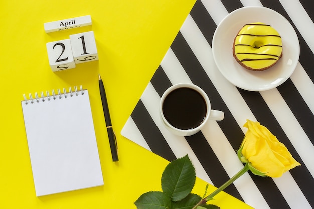 calendário 21 de abril. Xícara de café, rosquinha e rosa, o bloco de notas para o texto. Local de trabalho elegante conceito