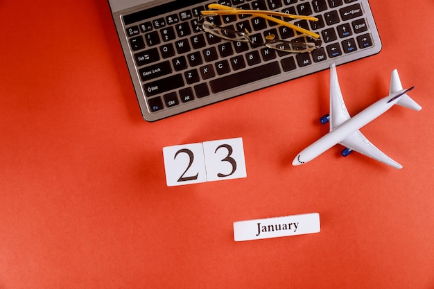 Calendario del 23 de enero con accesorios en el espacio de trabajo comercial escritorio de oficina en el teclado de la computadora, avión, gafas fondo rojo