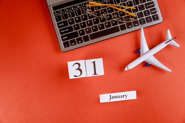 Calendario del 31 de enero con accesorios en el espacio de trabajo comercial escritorio de oficina en el teclado de la computadora, avión, gafas fondo rojo