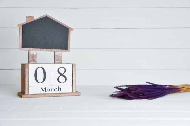 Calendario de bloque de madera del texto del 8 de marzo con la flor secada púrpura en el fondo de madera blanco.