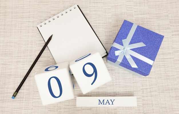 Calendário com texto azul na moda e números para 9 de maio e um presente em uma caixa.