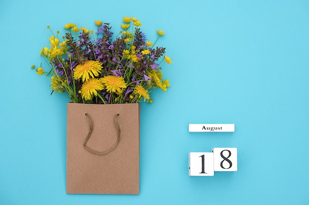 Calendario de cubos de madera 18 de agosto y campo coloridas flores rústicas en paquete artesanal sobre fondo azul.