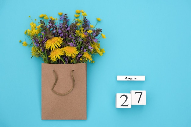 Calendario de cubos de madera el 27 de agosto y campo de coloridas flores rústicas en paquete artesanal en azul