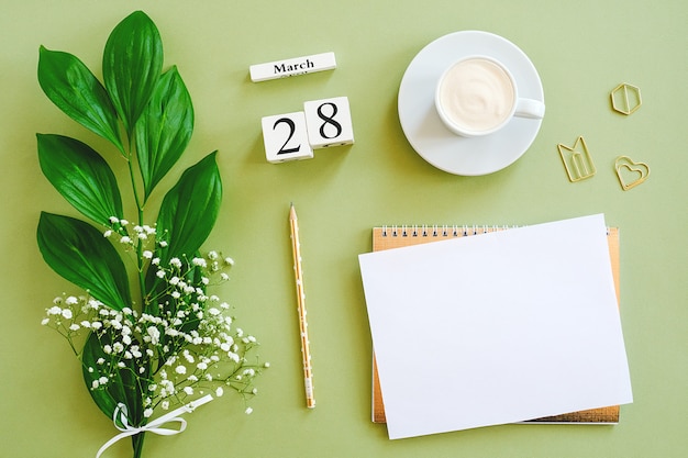 Calendario de cubos de madera 28 de marzo. Bloc de notas, taza de café, ramo de flores sobre fondo verde. Concepto hola primavera