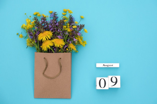 Calendario de cubos de madera el 9 de agosto y campo de coloridas flores rústicas en paquete artesanal en azul.