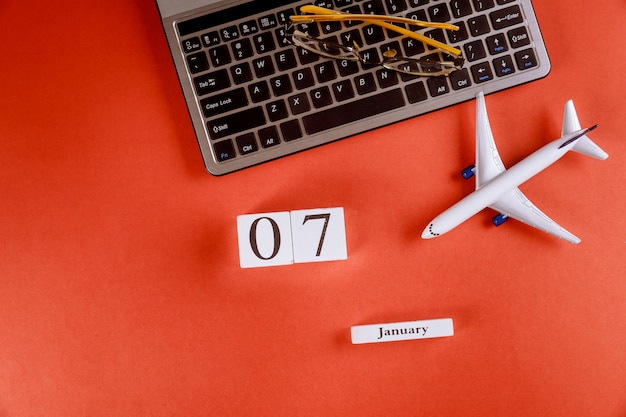 Calendário de 07 de janeiro com acessórios na mesa de escritório de espaço de trabalho de negócios no teclado do computador, avião, óculos fundo vermelho