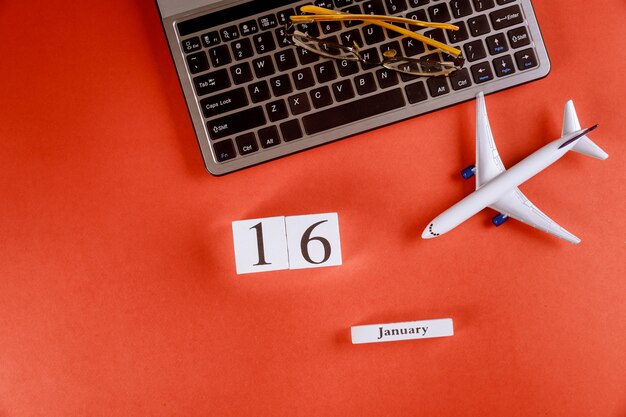 Calendário de 16 de janeiro com acessórios na mesa de escritório de espaço de trabalho de negócios no teclado do computador, avião, óculos fundo vermelho