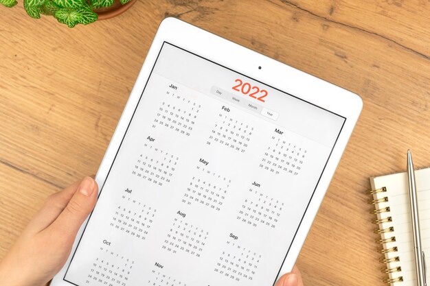 Calendário de 2022 na tela do computador tablet. Fundo de área de trabalho de mesa de madeira de negócios. Foto do conceito de planejamento de compromisso e reunião