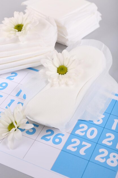 Calendário de absorventes higiênicos e flores brancas sobre fundo claro